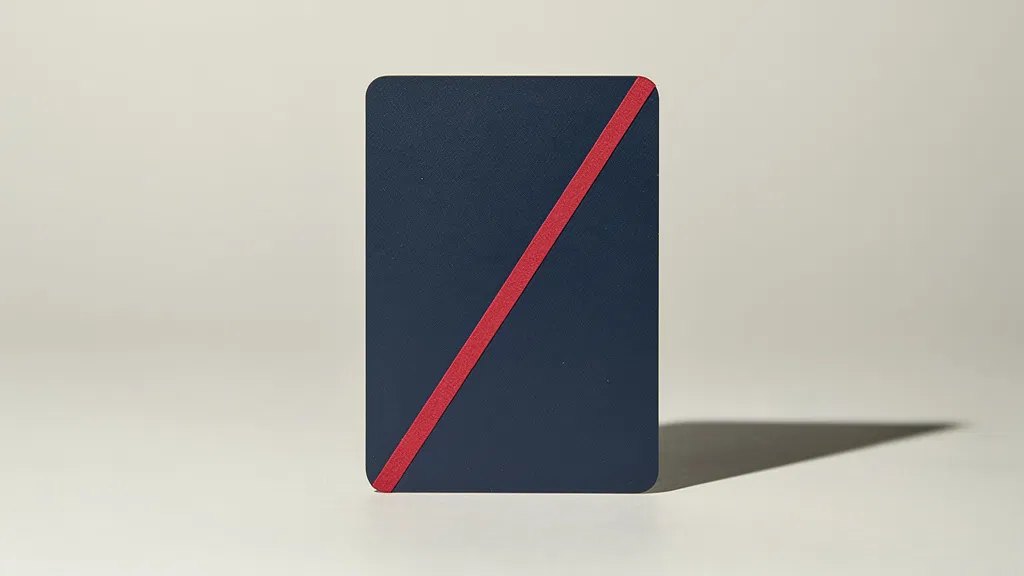 A blank matte navy card standing upright on a pale grey surface, with a single red stripe running diagonally across it.